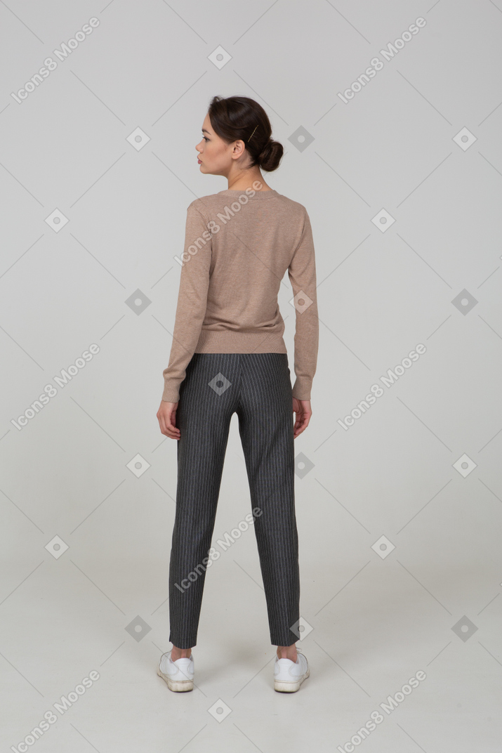 Back view of a young lady standing still in pullover and pants and turning head