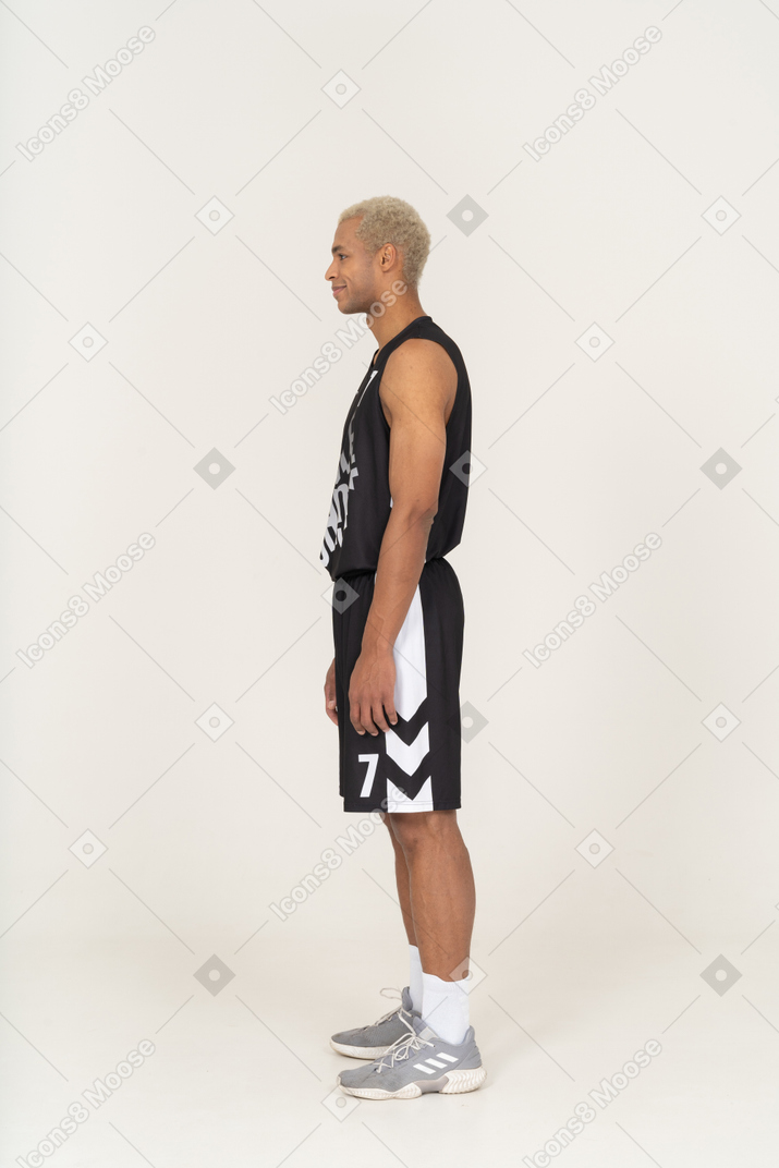 Vista lateral de um jovem jogador de basquete sorridente, parado
