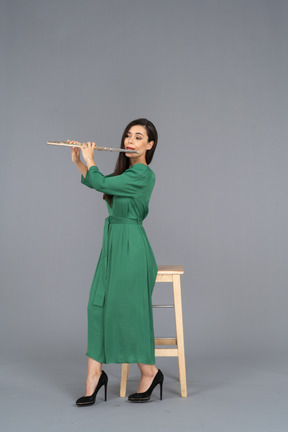 Вид сбоку на девушку в зеленом платье, сидящую на стуле и играющую на кларнете