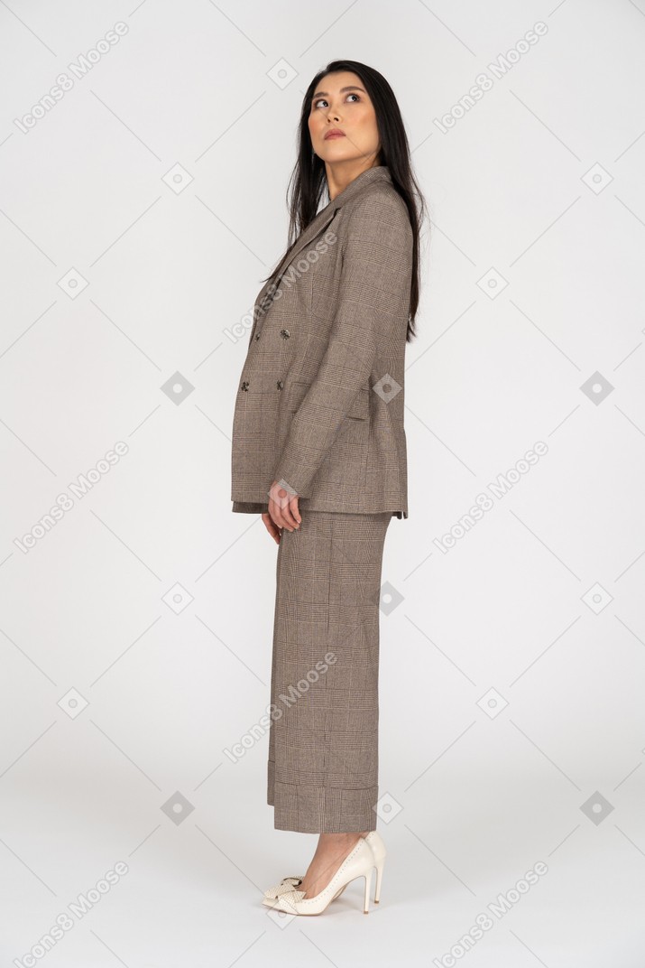 Вид сбоку молодой леди в коричневом деловом костюме, смотрящей вверх