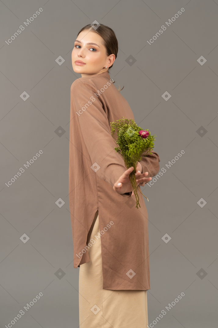 Giovane donna che tiene fiori dietro la schiena