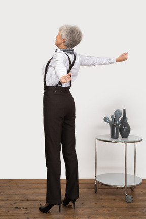 Three-quarter back view of an old lady in office clothing raising her hands
