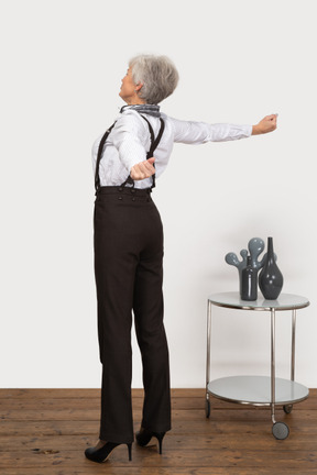 Vue arrière de trois quarts d'une vieille dame en vêtements de bureau en levant les mains