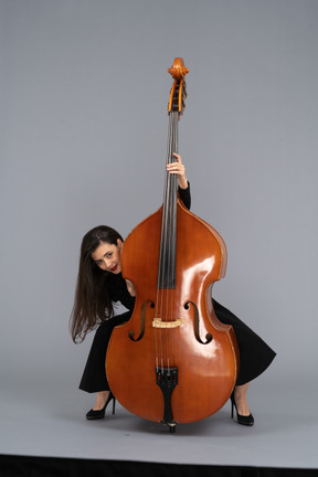 Front view of a crazy young lady squatting behind her double-bass