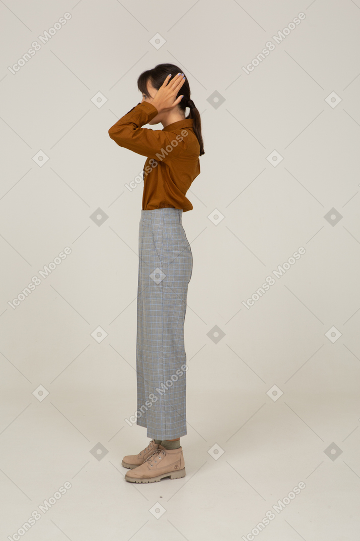 Side view of a young asian female in breeches and blouse touching head