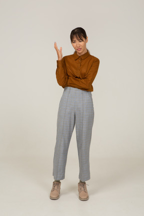 Vista frontal de uma jovem mulher asiática com calça e blusa, levantando a mão