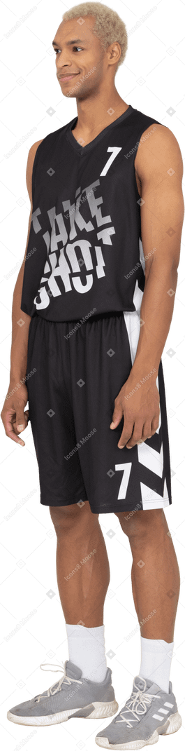 Vista di tre quarti di un giovane giocatore di basket maschio sorridente che sta fermo