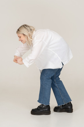 Side view of a blonde female in casual clothes showing a heart gesture while bending