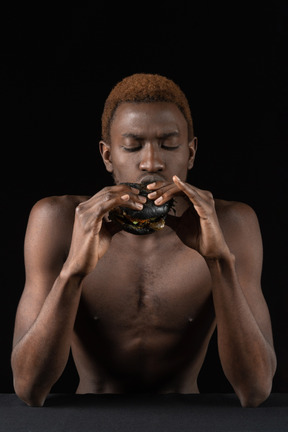 Vista frontal de un joven afro comiendo una hamburguesa