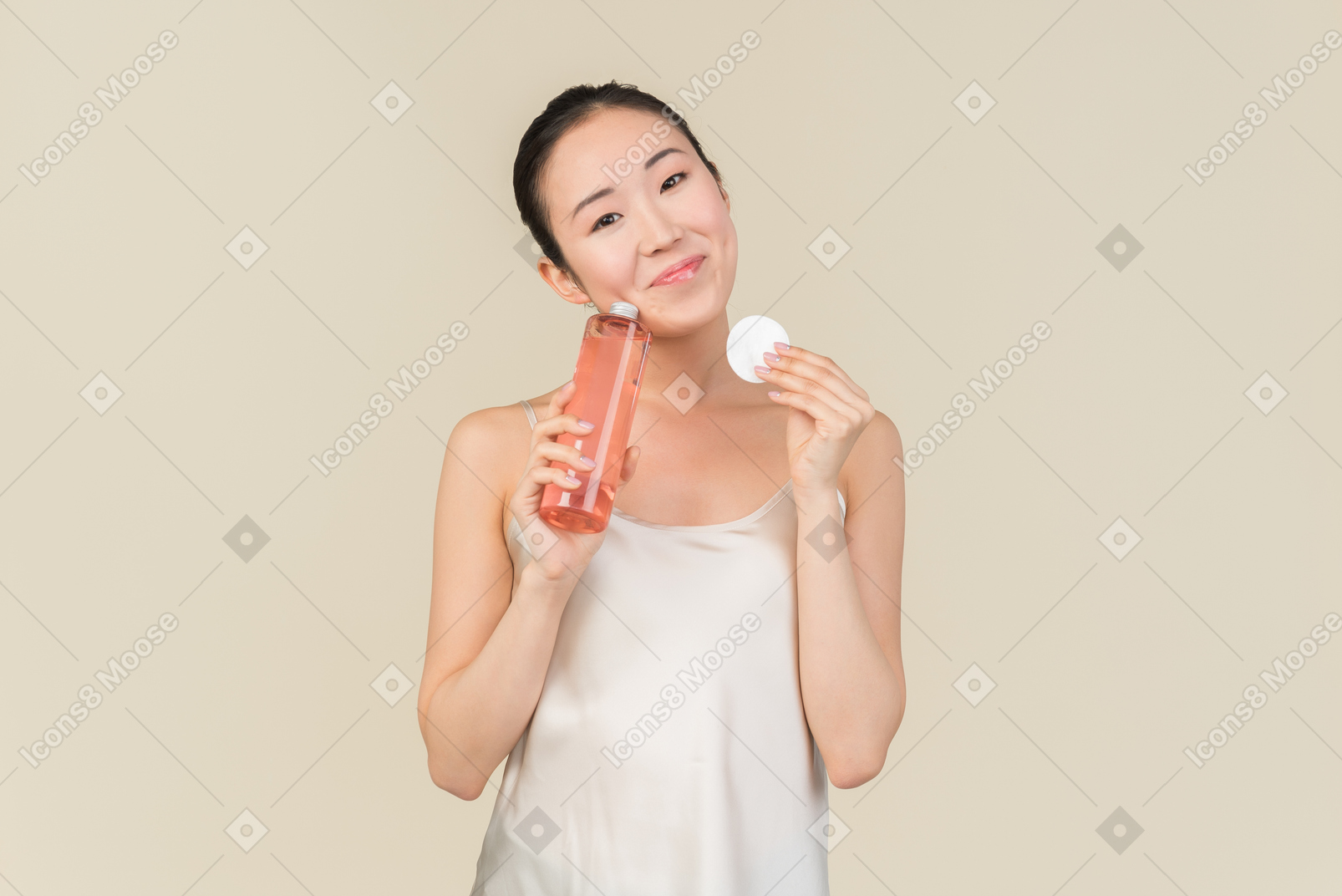 Мечтательная молодая азиатская девушка держит косметическую бутылку и ватный диск