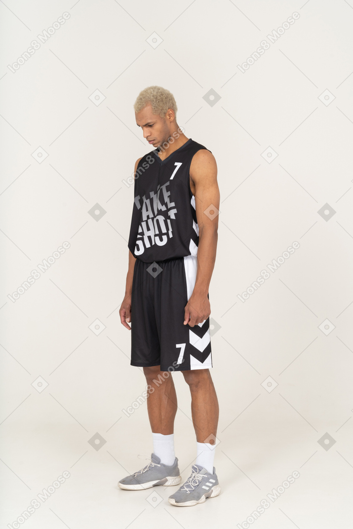 Three-quarter view of a serious young male basketball player looking down