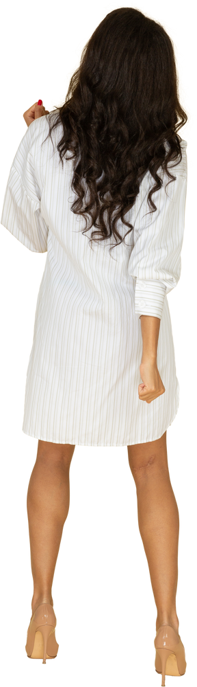 Vista posterior de una mujer joven de piel oscura con su vestido blanco levantando las manos
