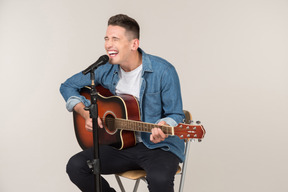 Laughing young guy singing and playing on a guitar