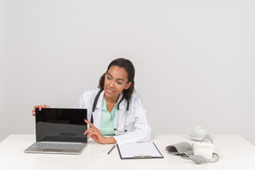 Confiante médico feminino mostrando algo em seu laptop