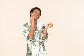 Young black short haired woman in a dressing gown, holding half of an avocado