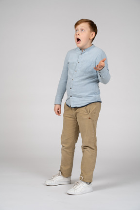 Surprised boy in blue shirt and khaki pants looking up