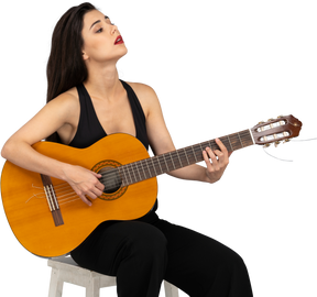 Dreiviertelansicht einer sitzenden jungen dame im schwarzen anzug, die die gitarre hält und den kopf hebt