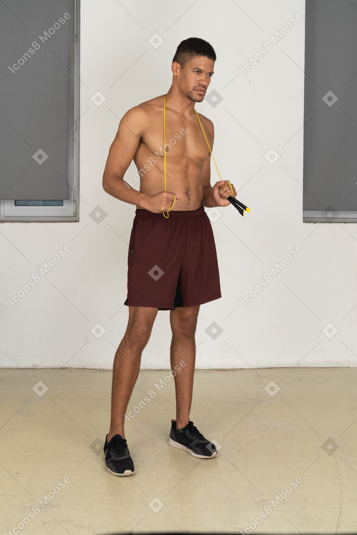 Bare chested man in sport shorts standing with jumping rope over his neck