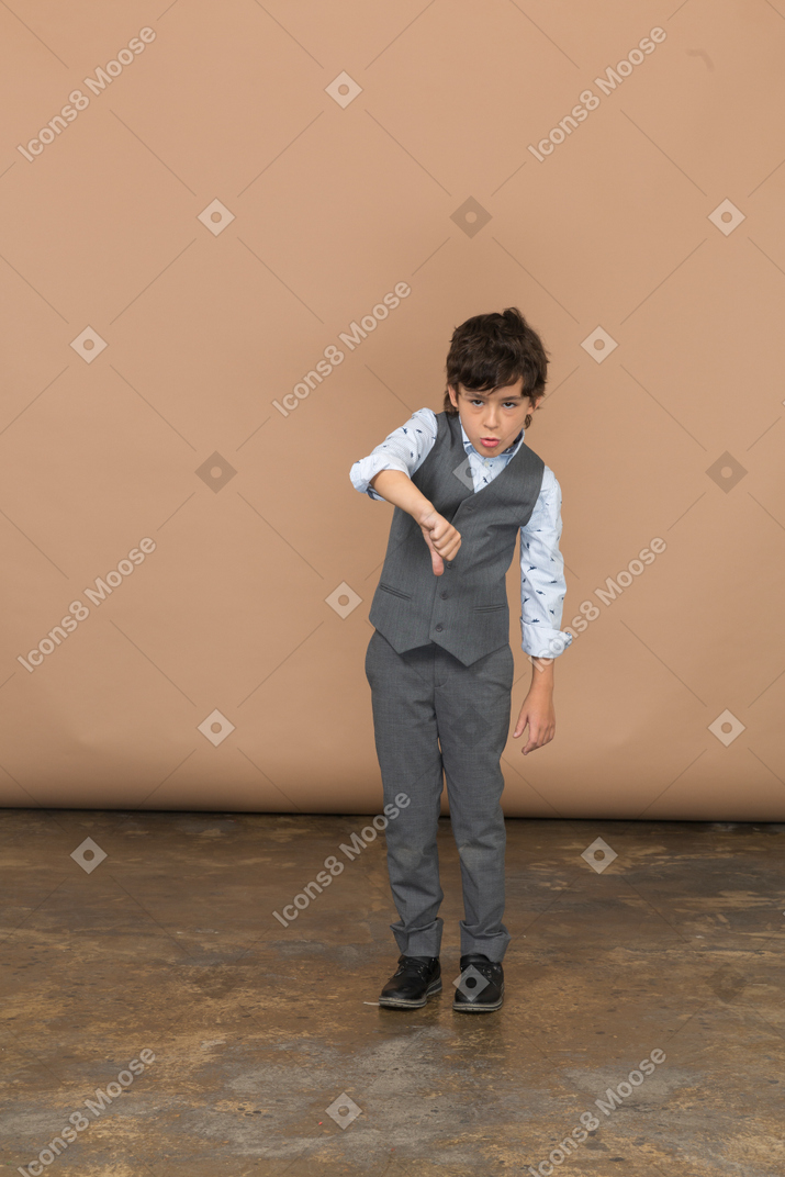 Vista frontal de un chico lindo con traje gris que muestra el pulgar hacia abajo
