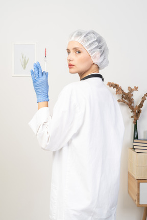 Vista posterior de tres cuartos de una joven doctora sosteniendo una jeringa