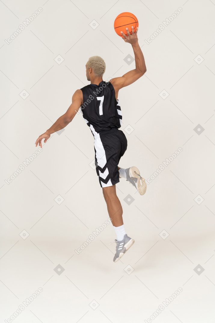 Vista posterior de tres cuartos de un joven jugador de baloncesto masculino anotando un punto