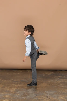 Side view of a boy in grey suit posing on one leg