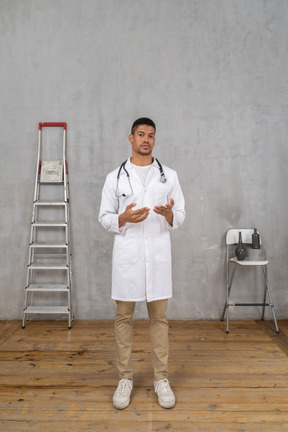 Front view of a young doctor standing in a room with ladder and chair explaining something