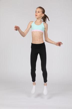 Vista frontal de una jovencita en ropa deportiva levantando las manos y mirando a un lado mientras salta
