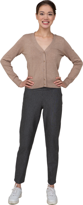 Vista frontale di una donna sorridente in pullover e pantaloni che mette le mani sui fianchi