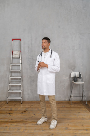 Vista di tre quarti di un giovane medico in piedi in una stanza con una scala e una sedia che si tengono per mano