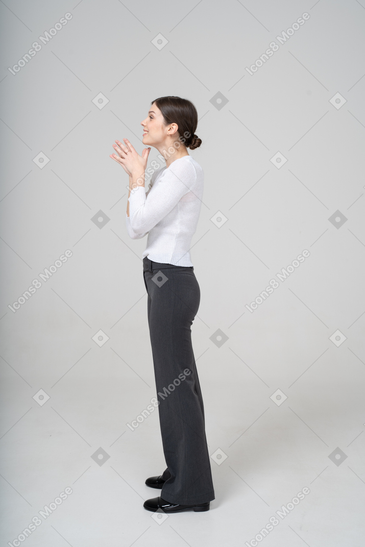 Вид сбоку молодой женщины в черных штанах и белой блузке жестикулируют