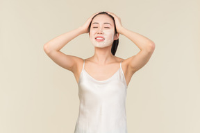 Relaxed young asian woman with facial mask touching head