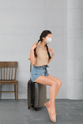 Mujer con mascarilla sentada en una maleta