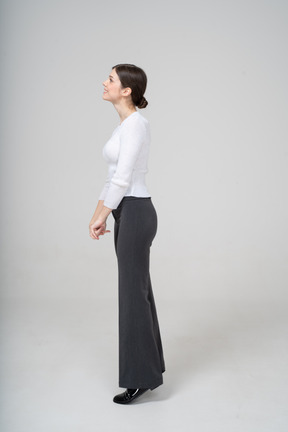 Вид сбоку молодой женщины в черных брюках и белой блузке, стоящей на носках