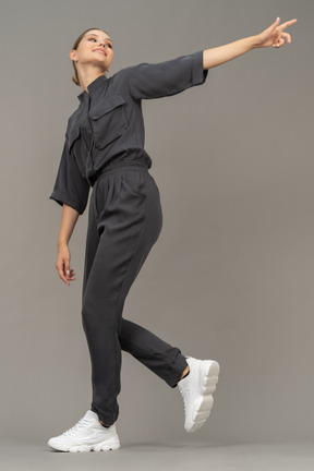 Side view of a cheerful young woman in a jumpsuit outstretching her arm