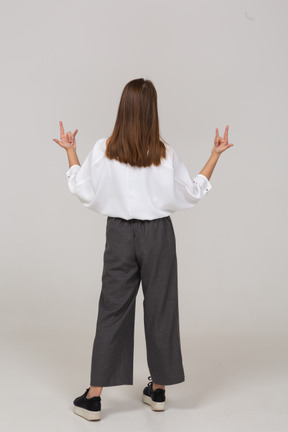 Vista posteriore di una giovane donna in abiti da ufficio che mostra il gesto rock