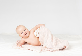 Smiling baby boy covered in beige knitted blanket