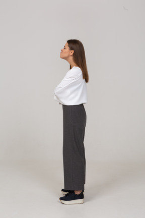 Vista lateral de uma jovem com uma careta em roupas de escritório, cruzando os braços