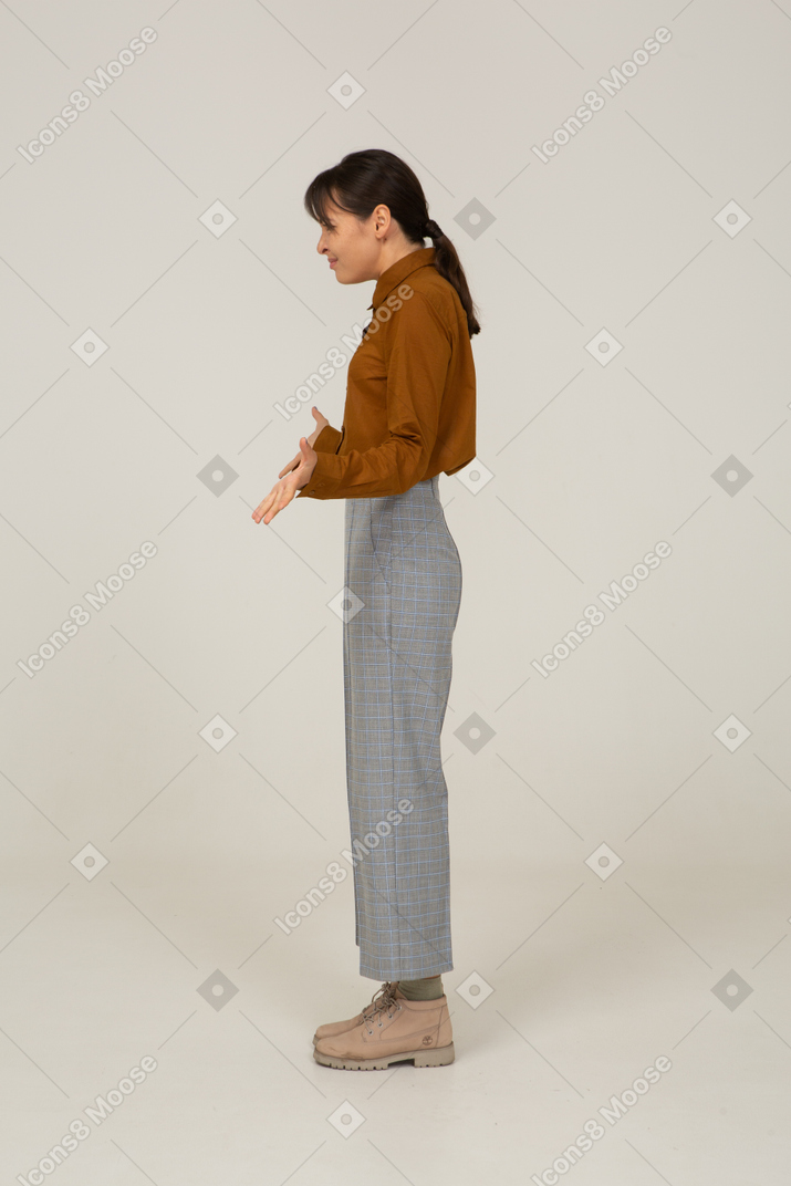Vista laterale di una giovane donna asiatica in calzoni e camicetta che allarga le braccia