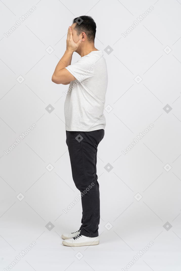 Seitenansicht eines mannes in freizeitkleidung, der das gesicht mit den händen bedeckt