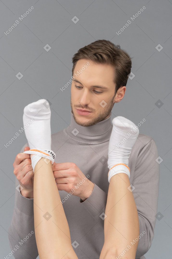 一个年轻人在女性的脚上穿袜子