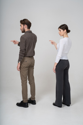Three-quarter back view of a young couple in office clothing pointing finger forward