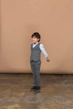 Vista frontal de um menino de terno em pé com o braço estendido