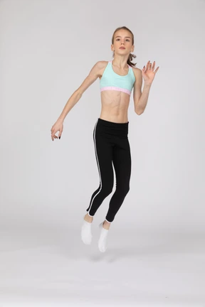 Three-quarter view of a teen girl in sportswear raising hand and jumping