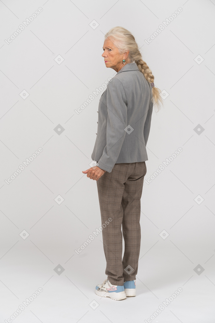 Rear view of an old woman in suit posing with hand on hip