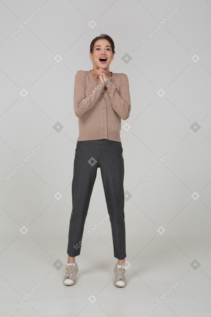 Front view of a delighted young lady in beige pullover holding hands together