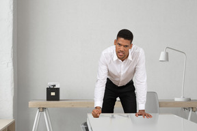 A man in a white shirt and black pants leaning over a desk