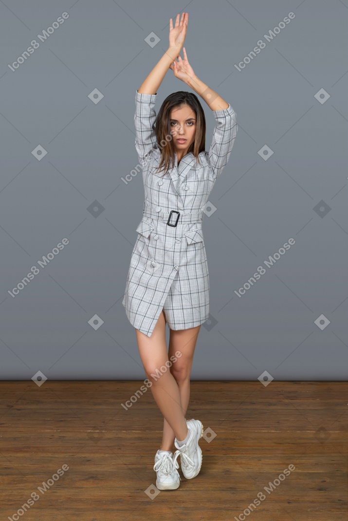 Attraente giovane donna in piedi con le braccia alzate e le gambe incrociate