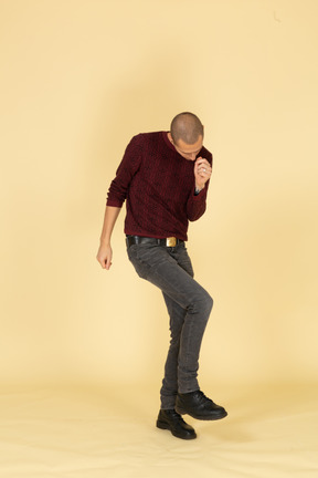 Front view of a dancing young man in red pullover raising leg