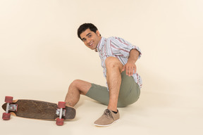 A nice-looking caucasian guy in a striped t-shirt, having fun learning how to ride a skateboard